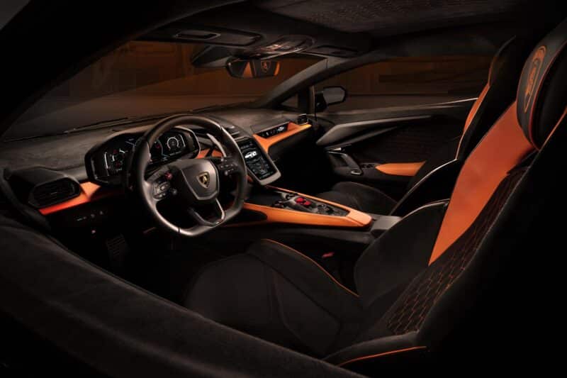 Siyah ve turuncu deri koltuklar, dijital ekranlı yüksek teknoloji kontrol paneli ve şık bir direksiyon simidi içeren Lamborghini Revuelto lüks spor otomobilin iç görünümü. En son özellikler, eşsiz bir sürüş deneyimi sağlayarak premium fiyatını yansıtır.