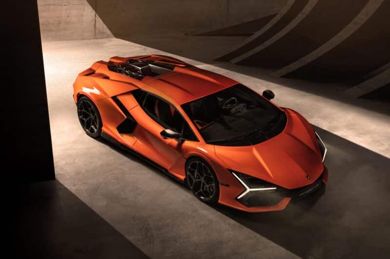 Bir turuncu Lamborghini Revuelto spor otomobili, etkileyici özelliklerini vurgulayan keskin açılar ve şık tasarım özellikleri sergileyen, yukarıdan izlenen iç mekanlarda park edilmiş.